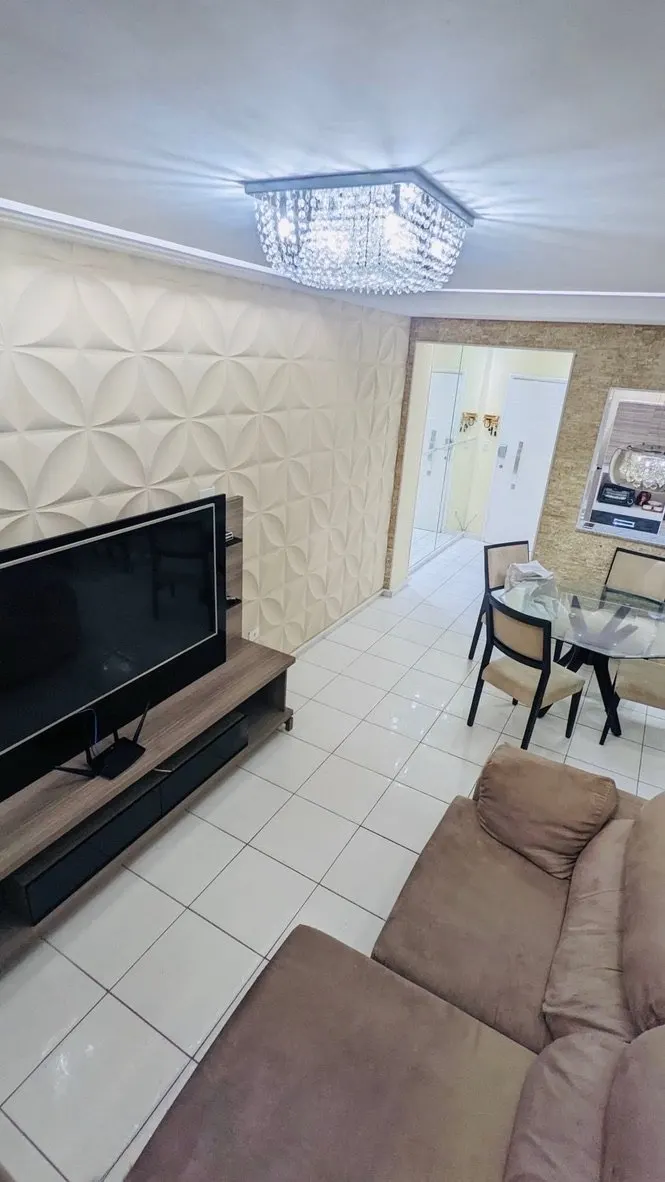 Sala com TV e sofá; ao fundo, mesa de jantar sob lustre de cristal