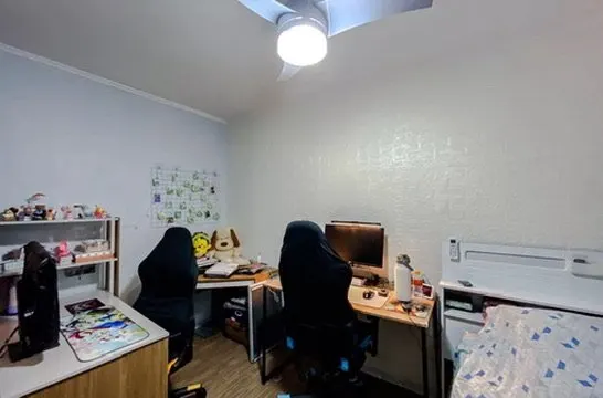 Quarto usado como escritório, com duas mesas e ventilador de teto